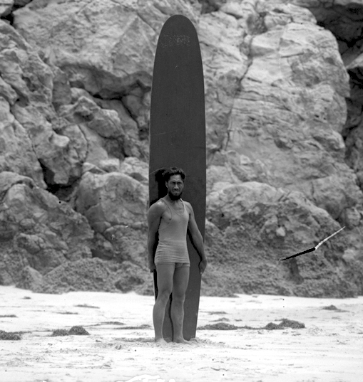 Duke Kahanamoku standing on beach with surfboard in Los Angeles, California, circa 1920