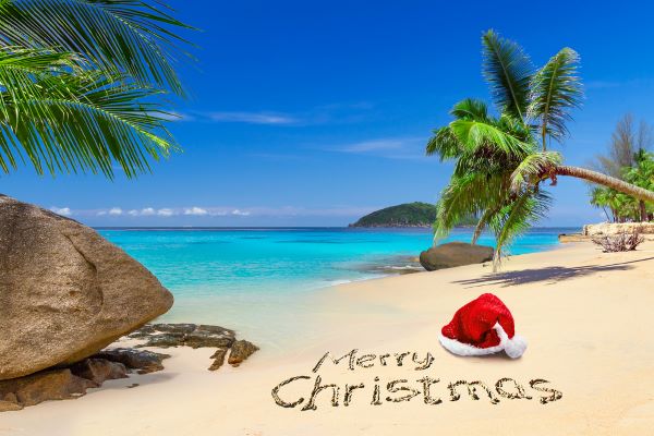 Merry Christma scrawled in the sand with Santa hat on the beach