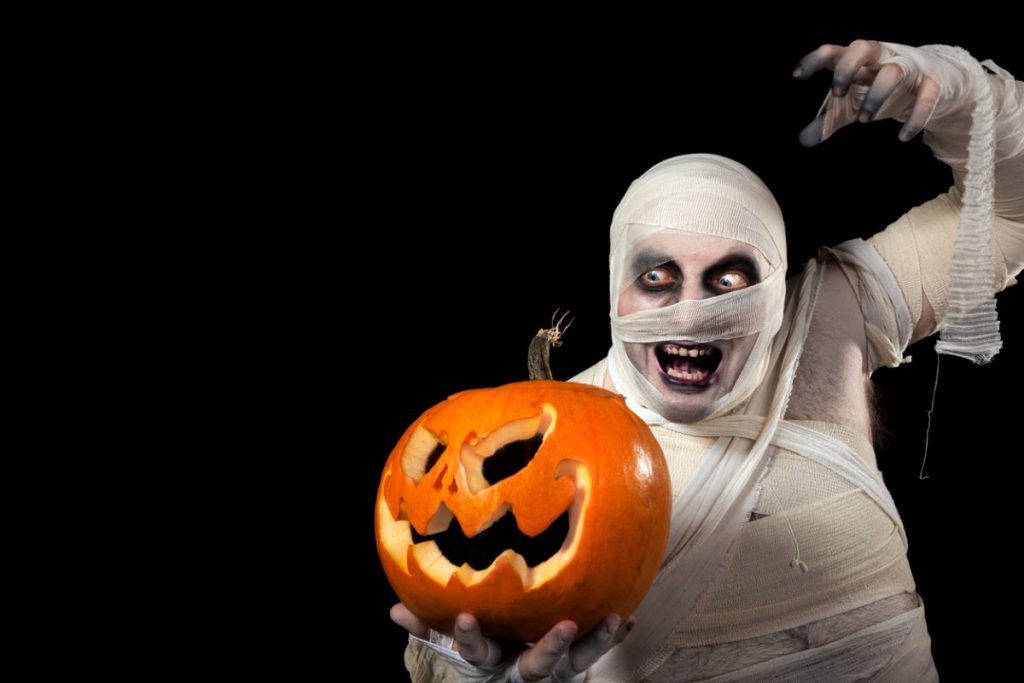 man in a DIY Halloween mummy costume holding a jack-o-lantern